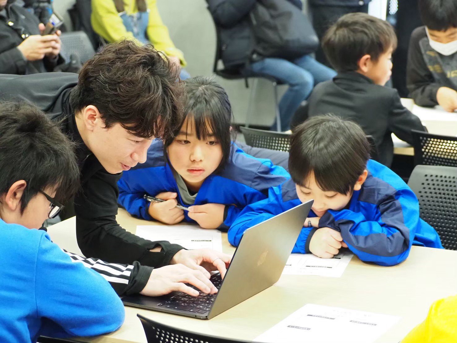 AIサッカークリニックの様子。子どもたちが講師と一緒にPCに向かい、AIと対話している風景。